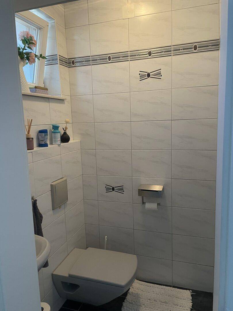 Kleines Gäste-WC mit wandhängendem WC, Waschbecken und Fenster für Belüftung.
