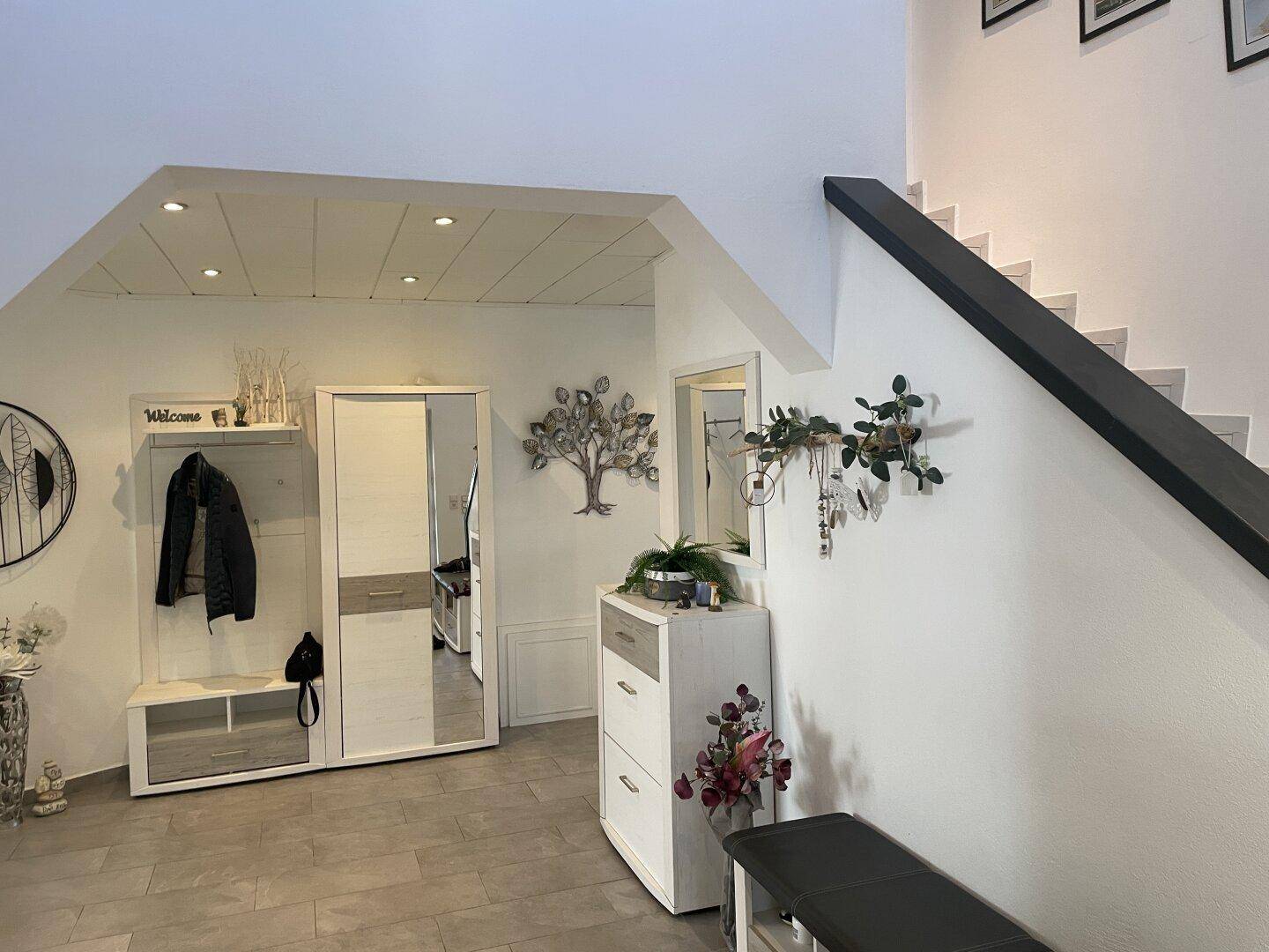 Heller Flur mit Treppe zum Obergeschoss, Garderobe und dekorativen Elementen.
