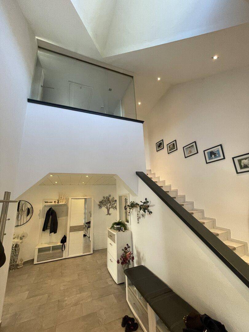 Heller Eingangsbereich mit offener Treppe, Galerie und hohen Decken.
