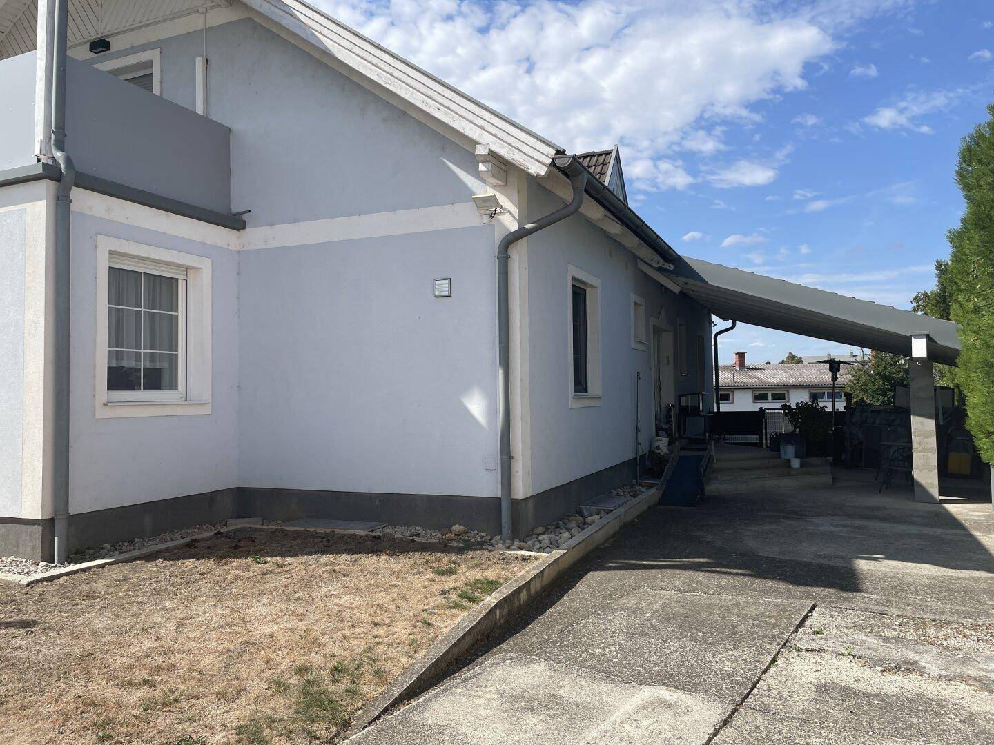 Seitenansicht des Hauses mit Carport, Gartenbereich und Balkon im Obergeschoss.