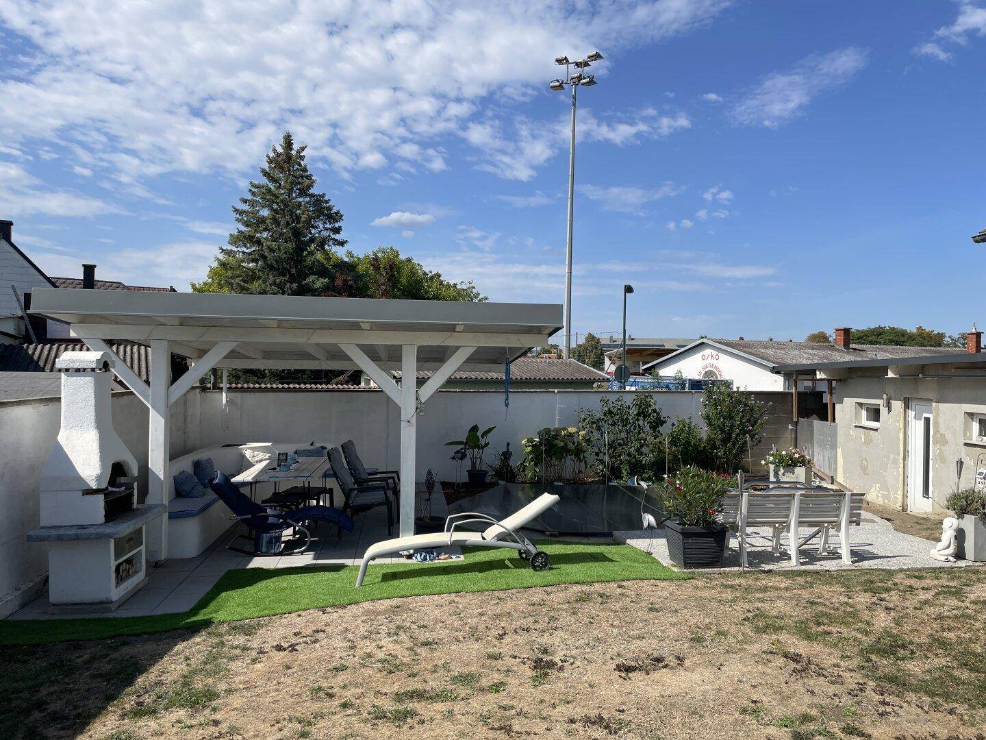 Großer Gartenbereich mit überdachtem Sitzbereich, Grillplatz und Liegestühlen.