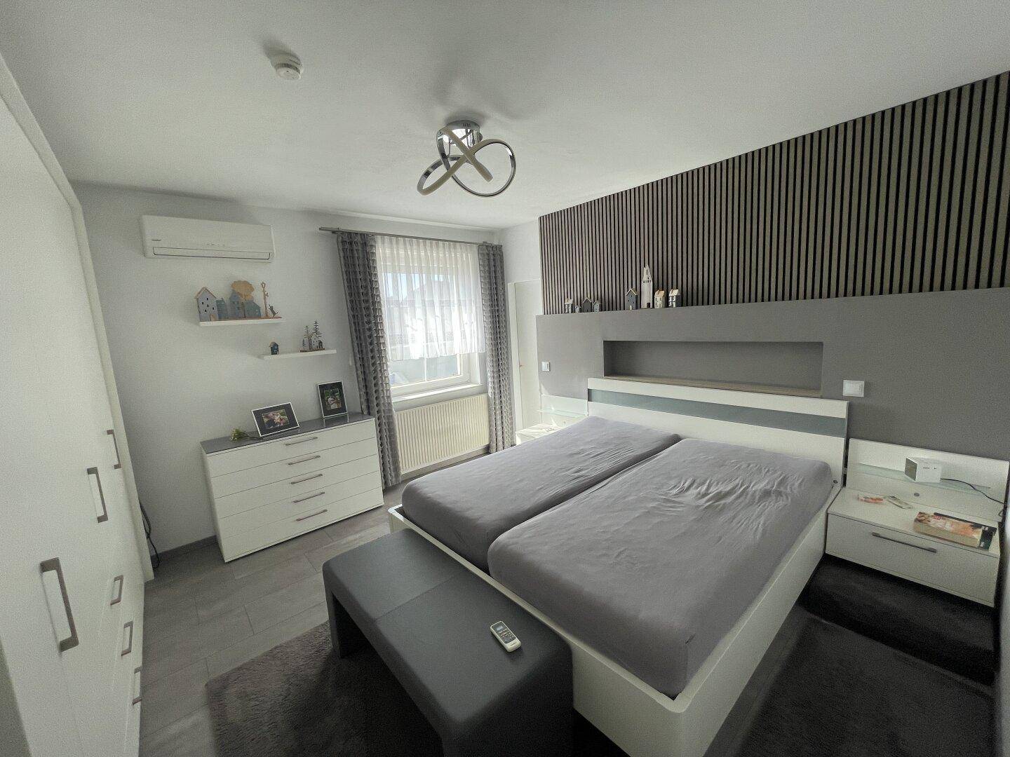 Modernes Schlafzimmer mit Doppelbett, Holzlamellenwand und Klimaanlage für angenehmes Klima.