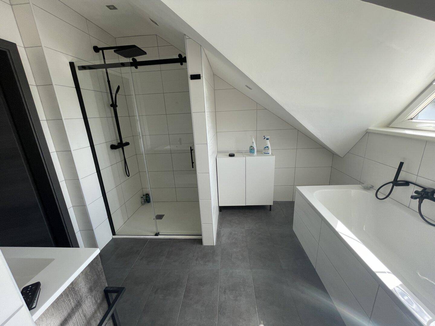 Modernes Badezimmer im Dachgeschoss mit Dusche, Badewanne und dunklen Armaturen.