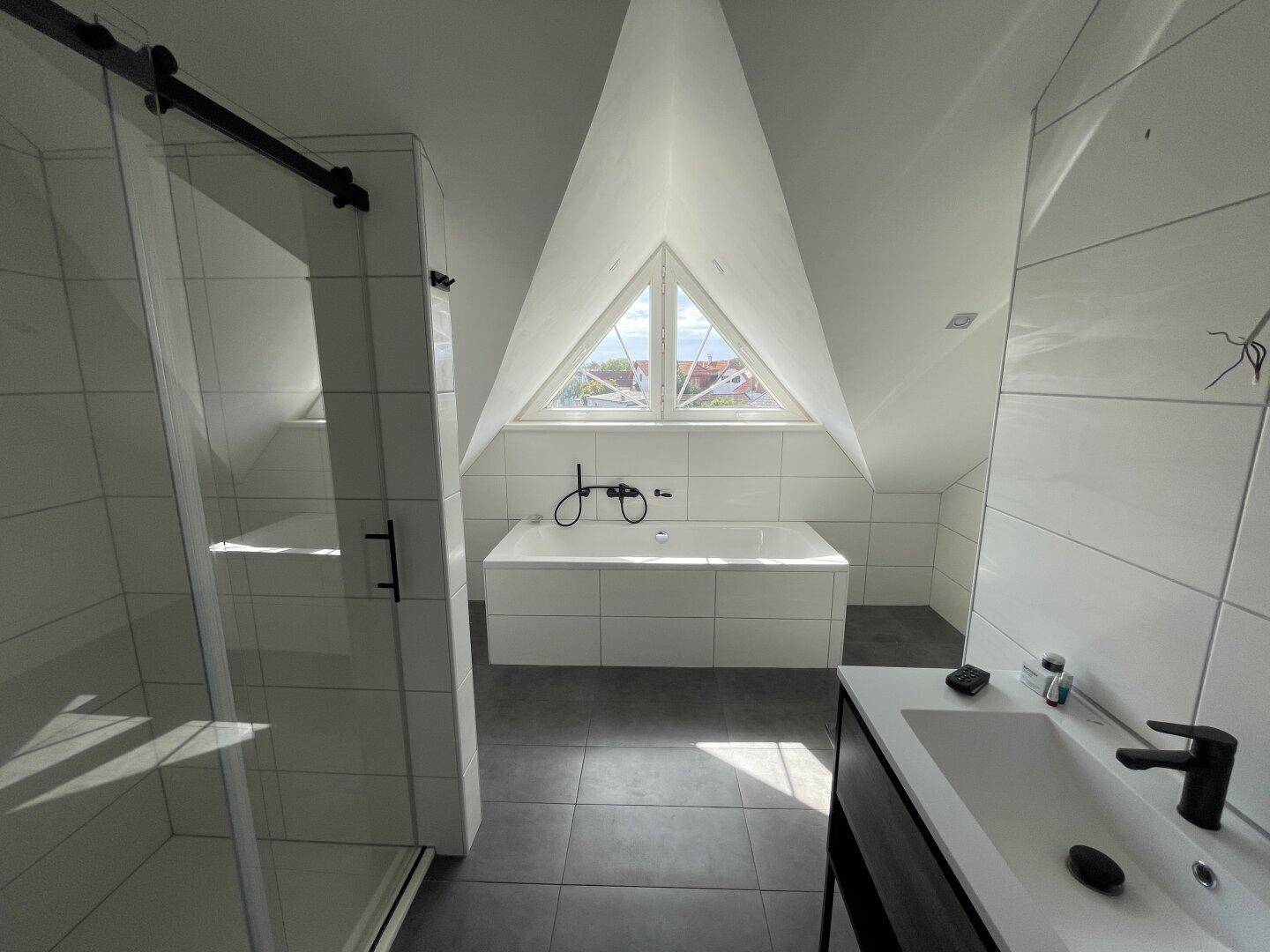 Helles Badezimmer mit Badewanne, begehbarer Dusche und dreieckigem Dachfenster für viel Tageslicht.