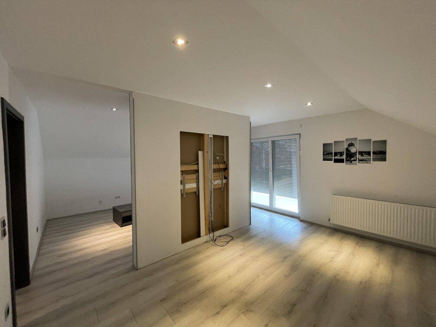 Heller Dachraum mit Laminatboden und vorbereiteter Wandinstallation für Unterhaltungselektronik.