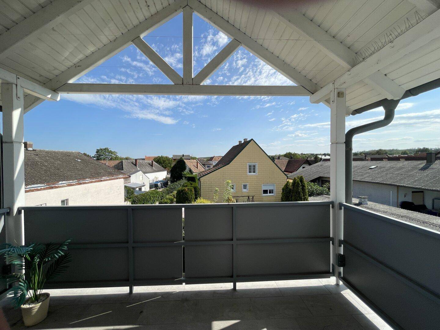 Überdachter Balkon mit Blick auf die umliegenden Häuser und den blauen Himmel, ideal zum Entspannen.