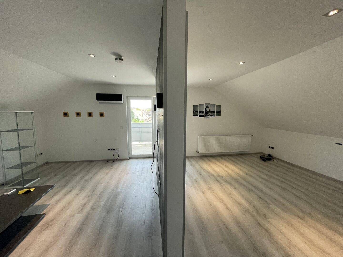 Geräumiges Dachzimmer mit Laminatboden, Klimaanlage und Zugang zu einem kleinen Balkon.
