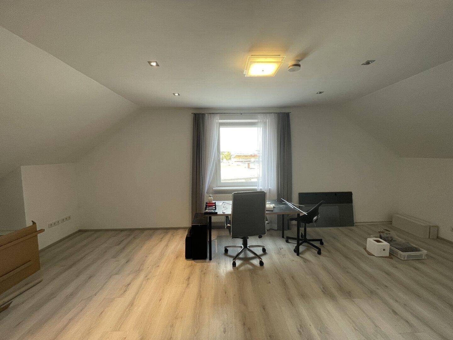 Helles Dachzimmer mit Schreibtisch, Bürostühlen und schrägen Wänden, ideal als Arbeitsbereich.