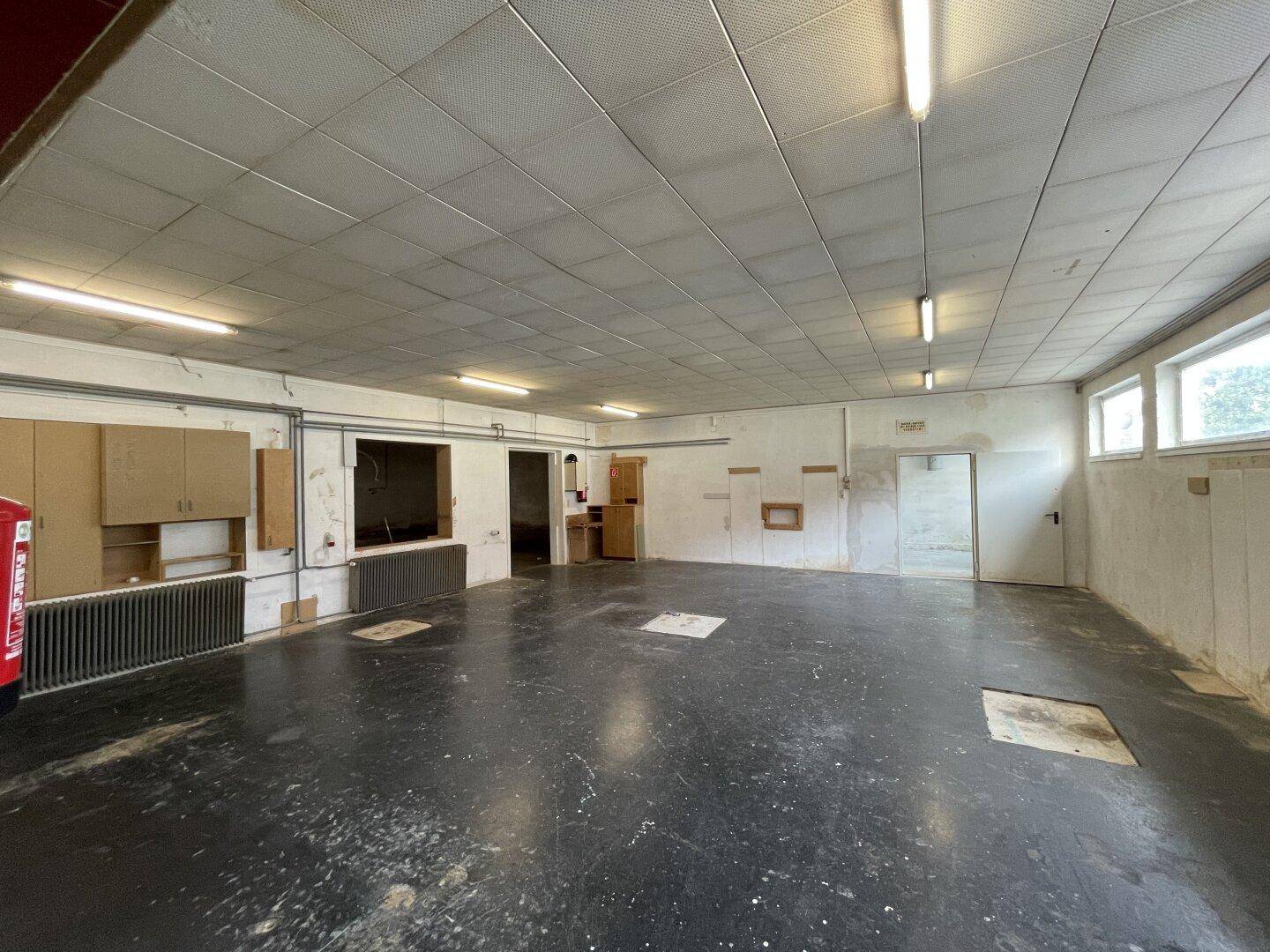 Großer leerer Raum mit dunklem Boden, Rasterdecke und Leuchtstoffröhren, bereit zur Nutzung.