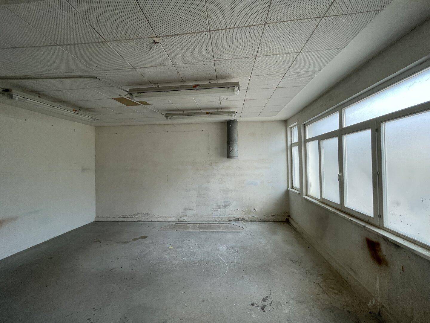 Kleiner, heller Raum mit großen Fenstern und Betonboden, geeignet als Büro oder Lager.