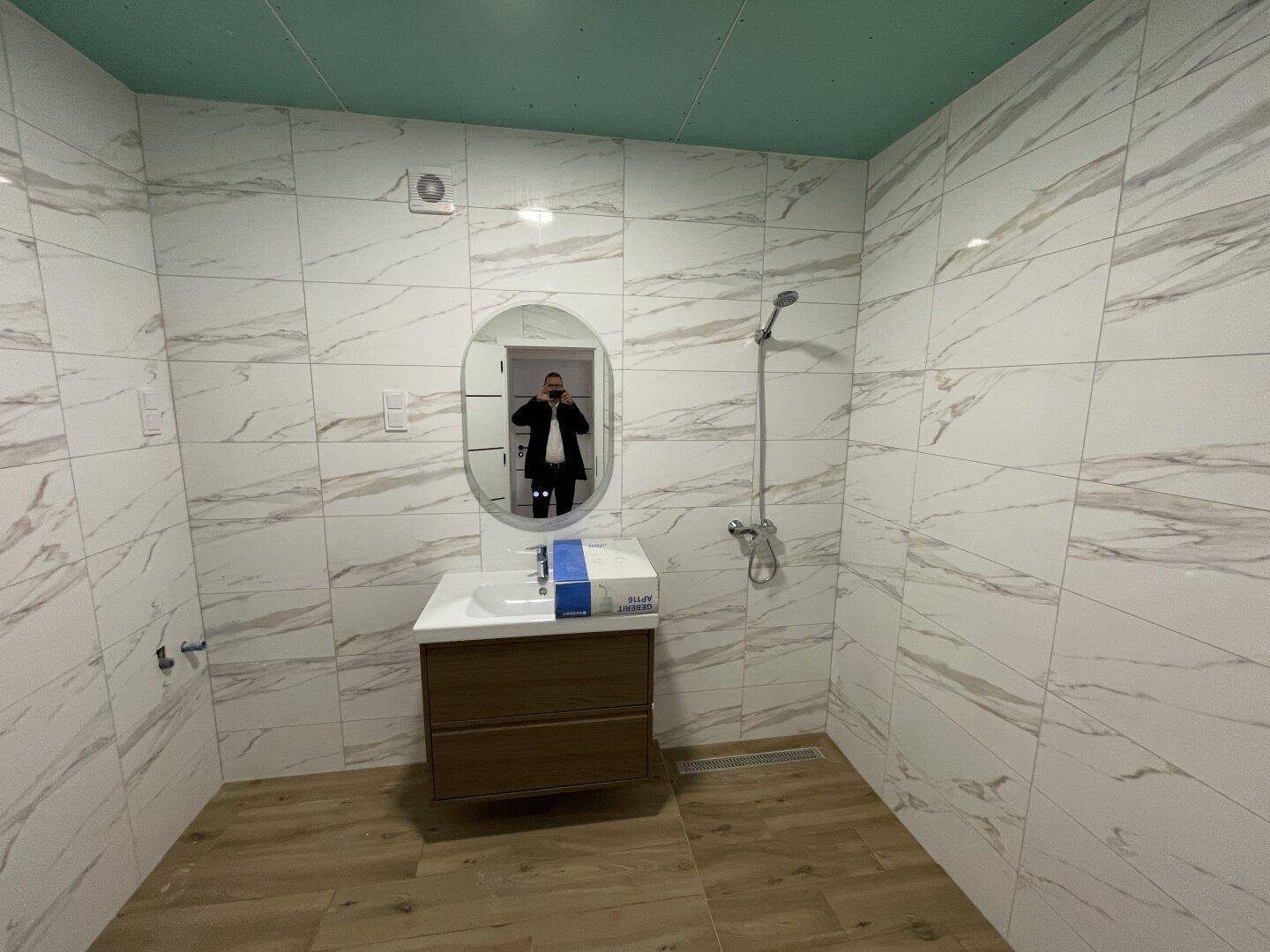 Modernes Badezimmer mit weißen Marmorfliesen, schwebendem Waschtisch und Duschbereich.