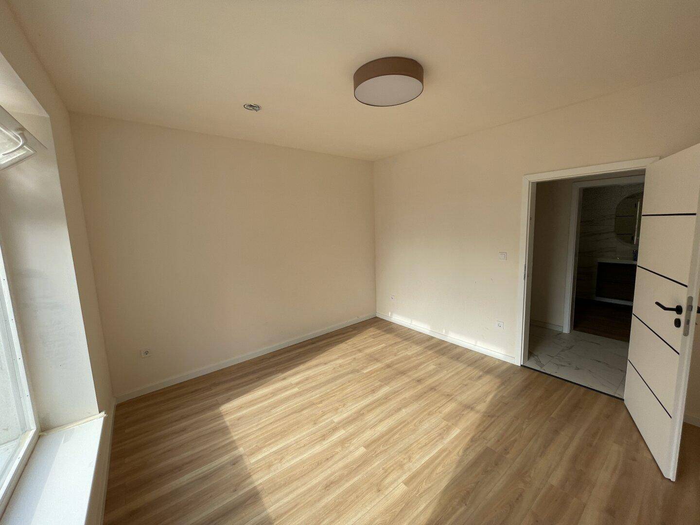 Helles Schlafzimmer mit Laminatboden und Zugang zu einem modernen Badezimmer.