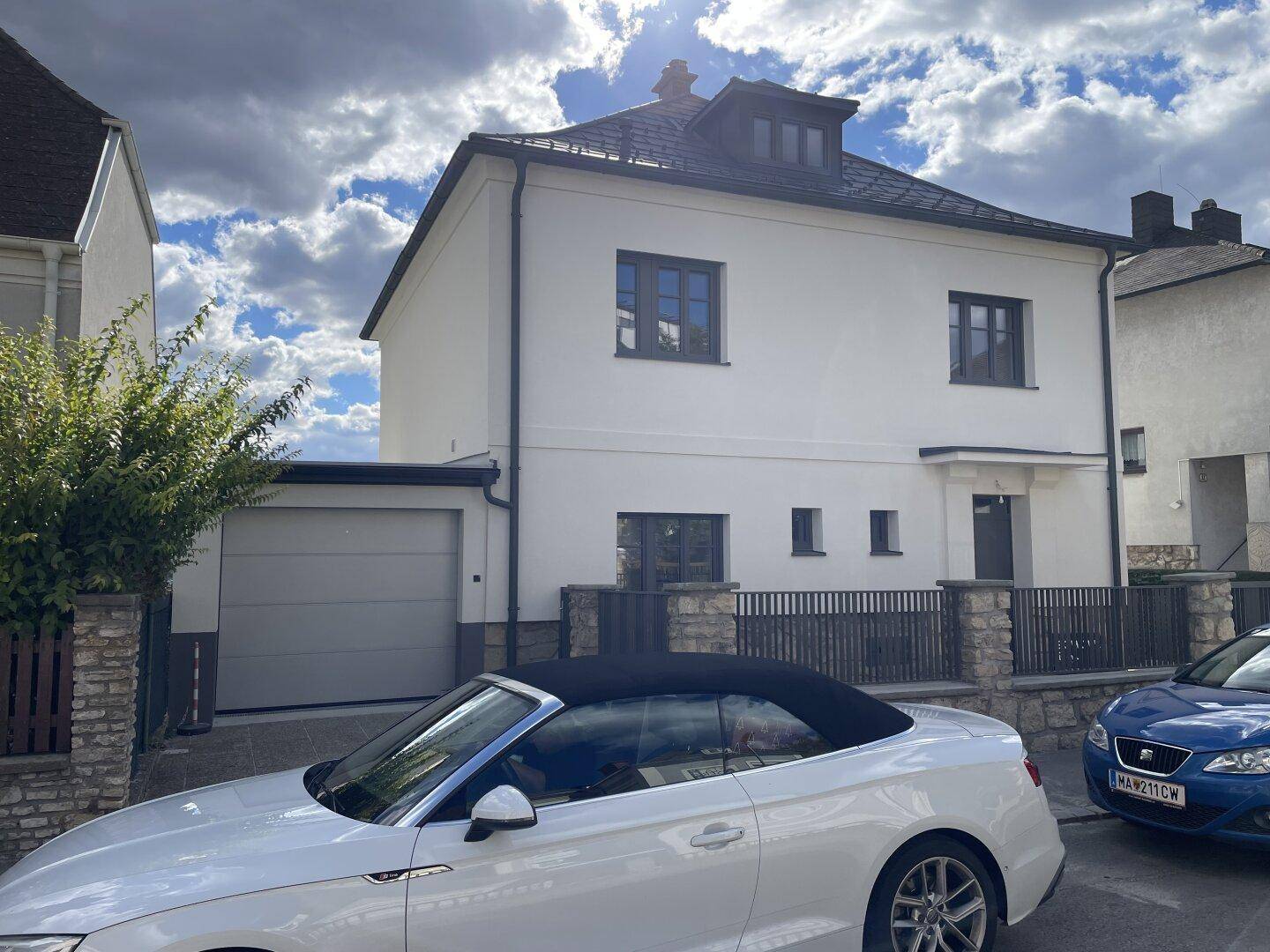 Ansicht der Hausfront mit integrierter Garage, Eingangsbereich und einem geparkten Cabriolet.