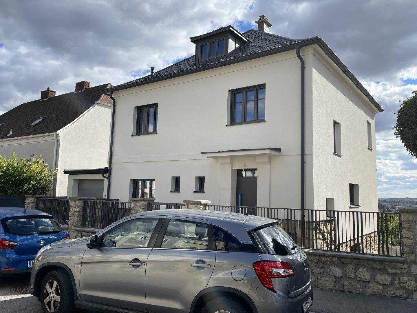 Ansicht der modernen Hausfassade mit Eingangsbereich und geparktem Auto auf der Straße.