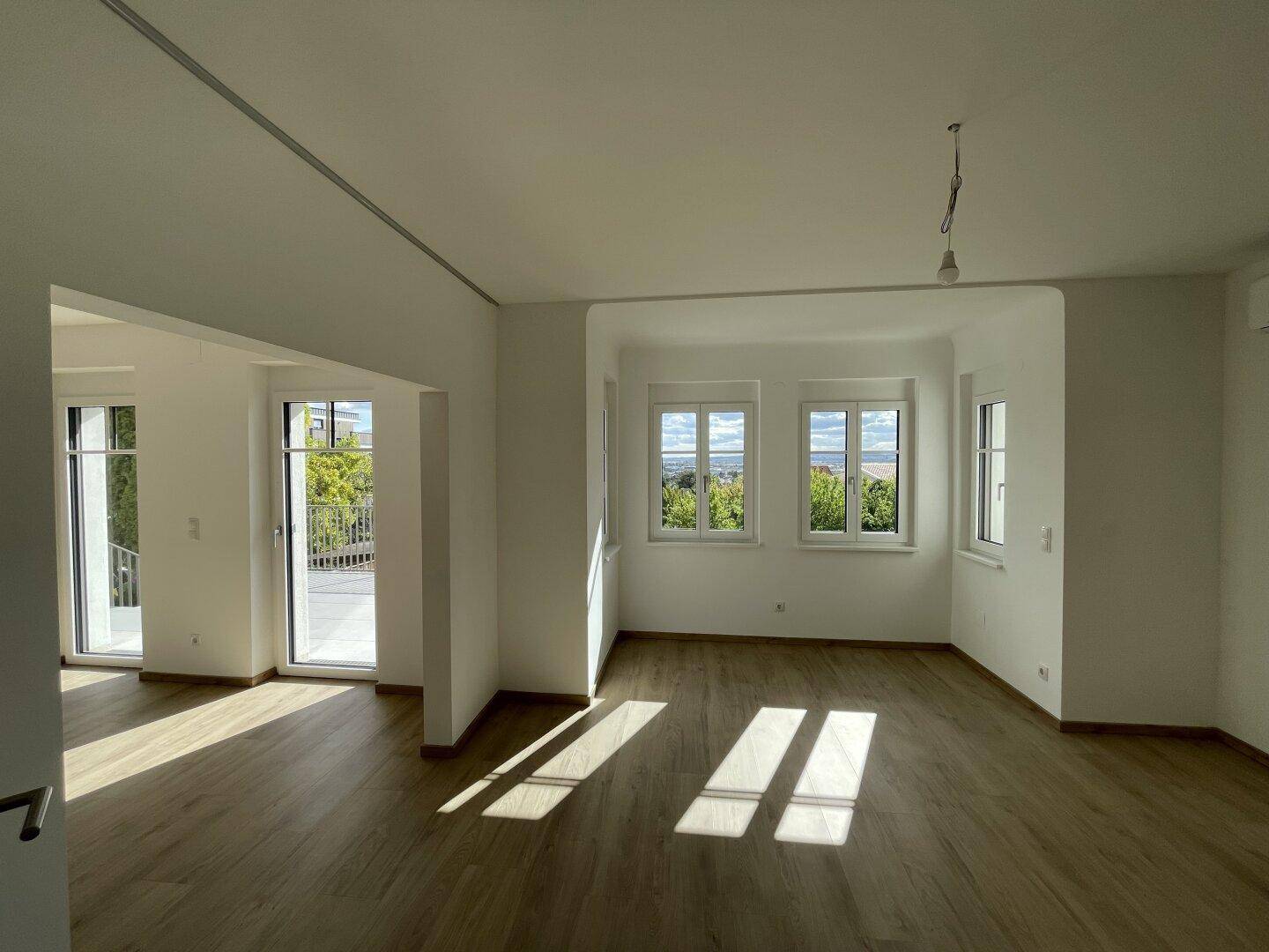 Lichtdurchflutetes Wohnzimmer mit Holzboden und Zugang zu einem Außenbereich, ideal für entspannte Stunden.