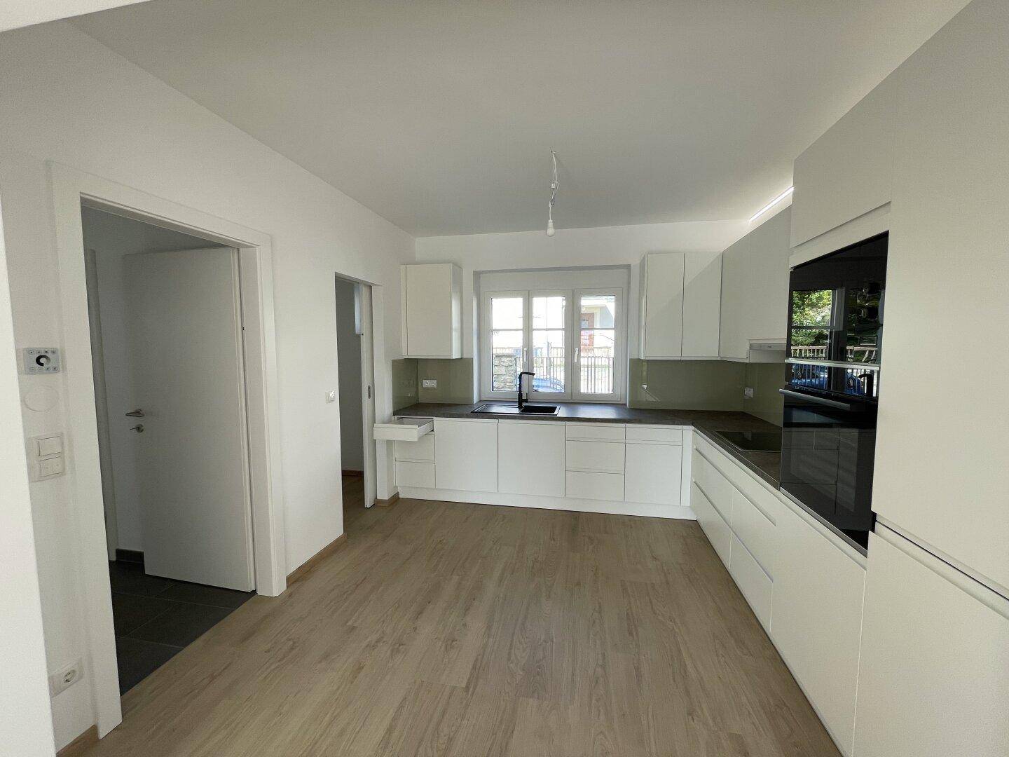 Moderne, unmöblierte Küche mit weißen Schränken, Spüle und Fenster, bereit für die individuelle Gestaltung.