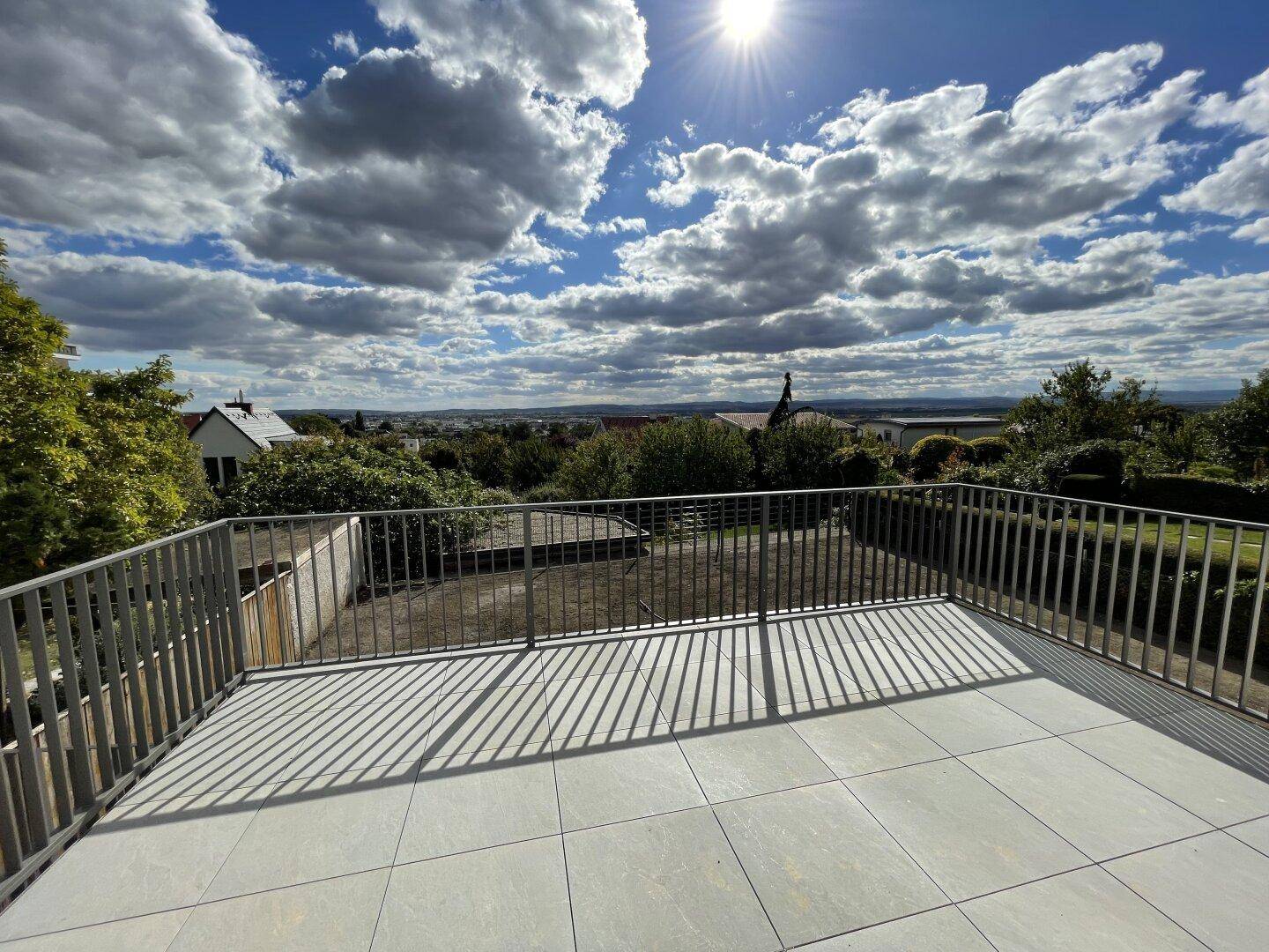 Große geflieste Terrasse mit Metallgeländer und weitem Blick über die Landschaft an einem sonnigen Tag.
