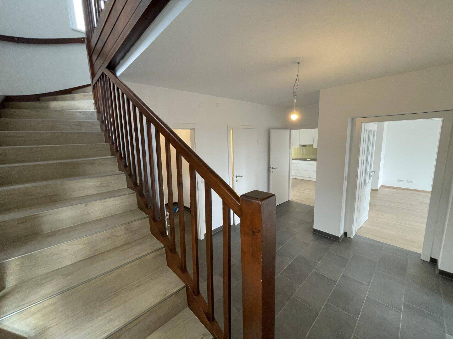 Geräumiger Flur mit dunklen Fliesen und einer eleganten Holztreppe, die in die oberen Stockwerke führt.