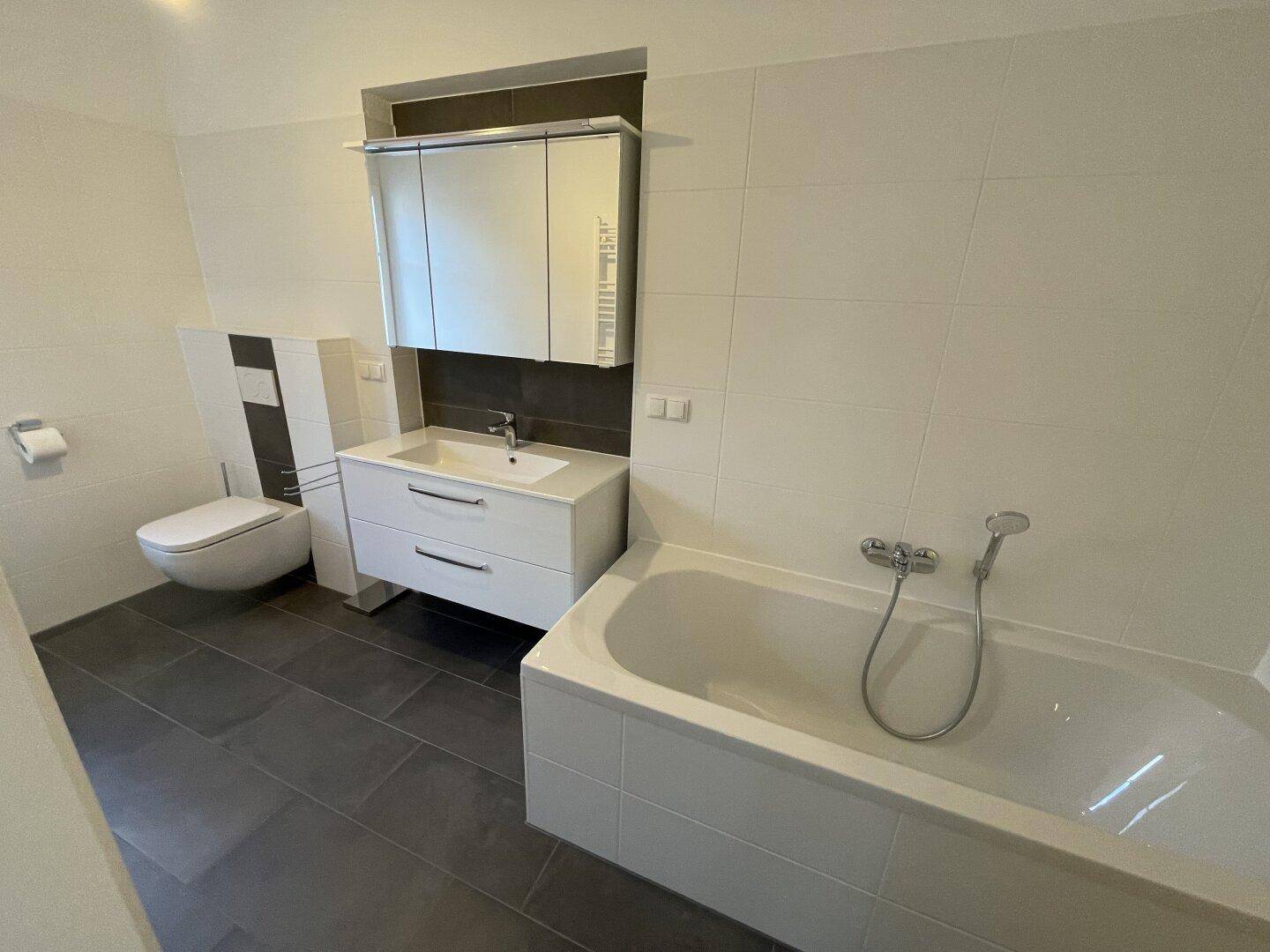 Modernes Badezimmer mit weißen Wandfliesen, Badewanne, wandhängendem WC und Waschtisch mit Spiegelschrank.