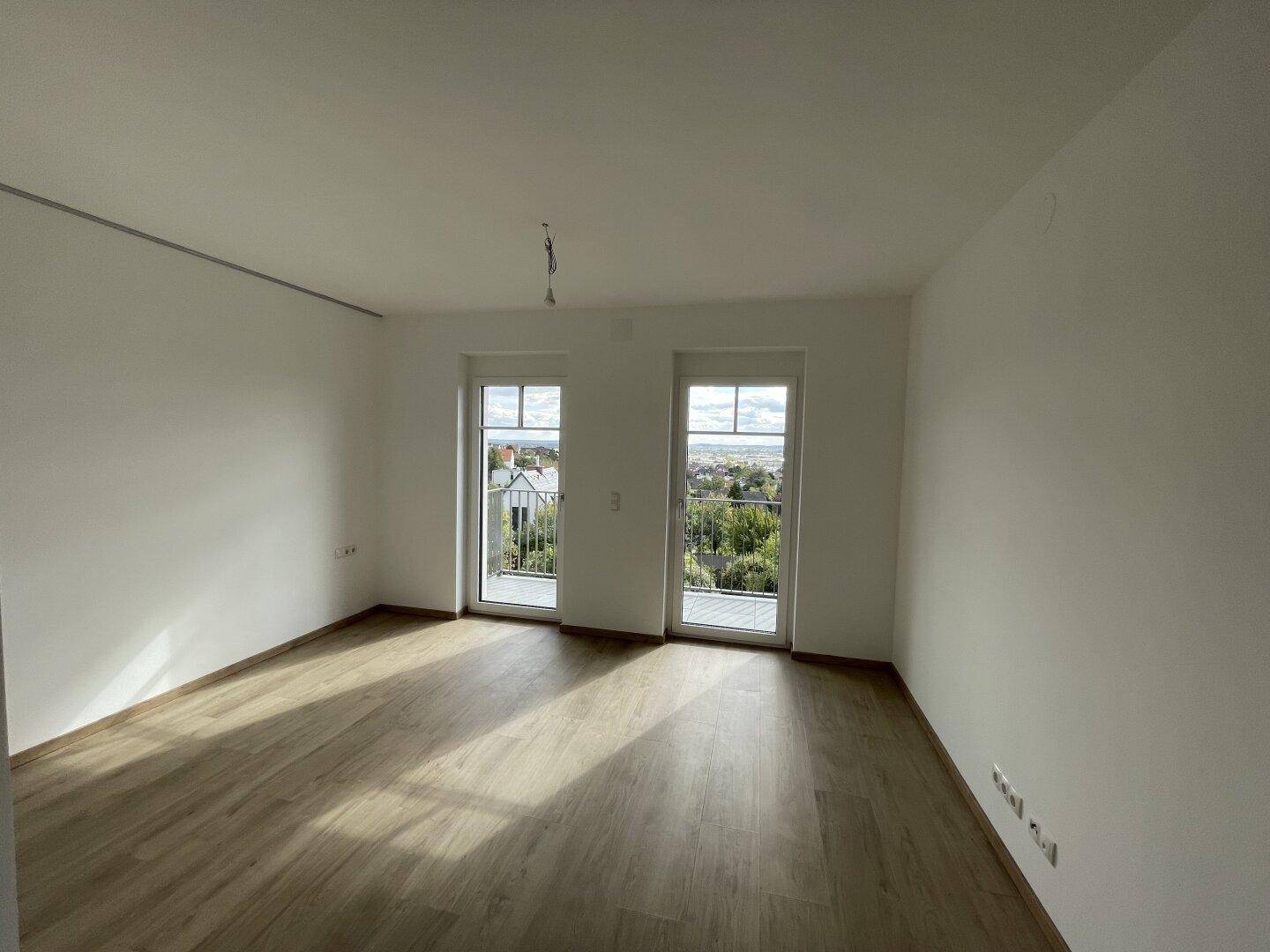 Helles Schlafzimmer mit Holzboden und zwei großen Glastüren, die Zugang zu einem Balkon bieten.