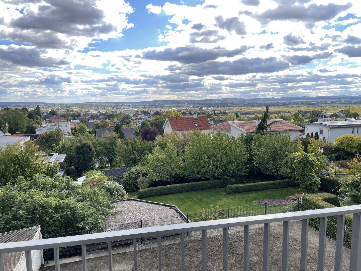 Weitläufiger Blick von einem Balkon auf einen gepflegten Garten mit Hecken und die umliegende Landschaft.