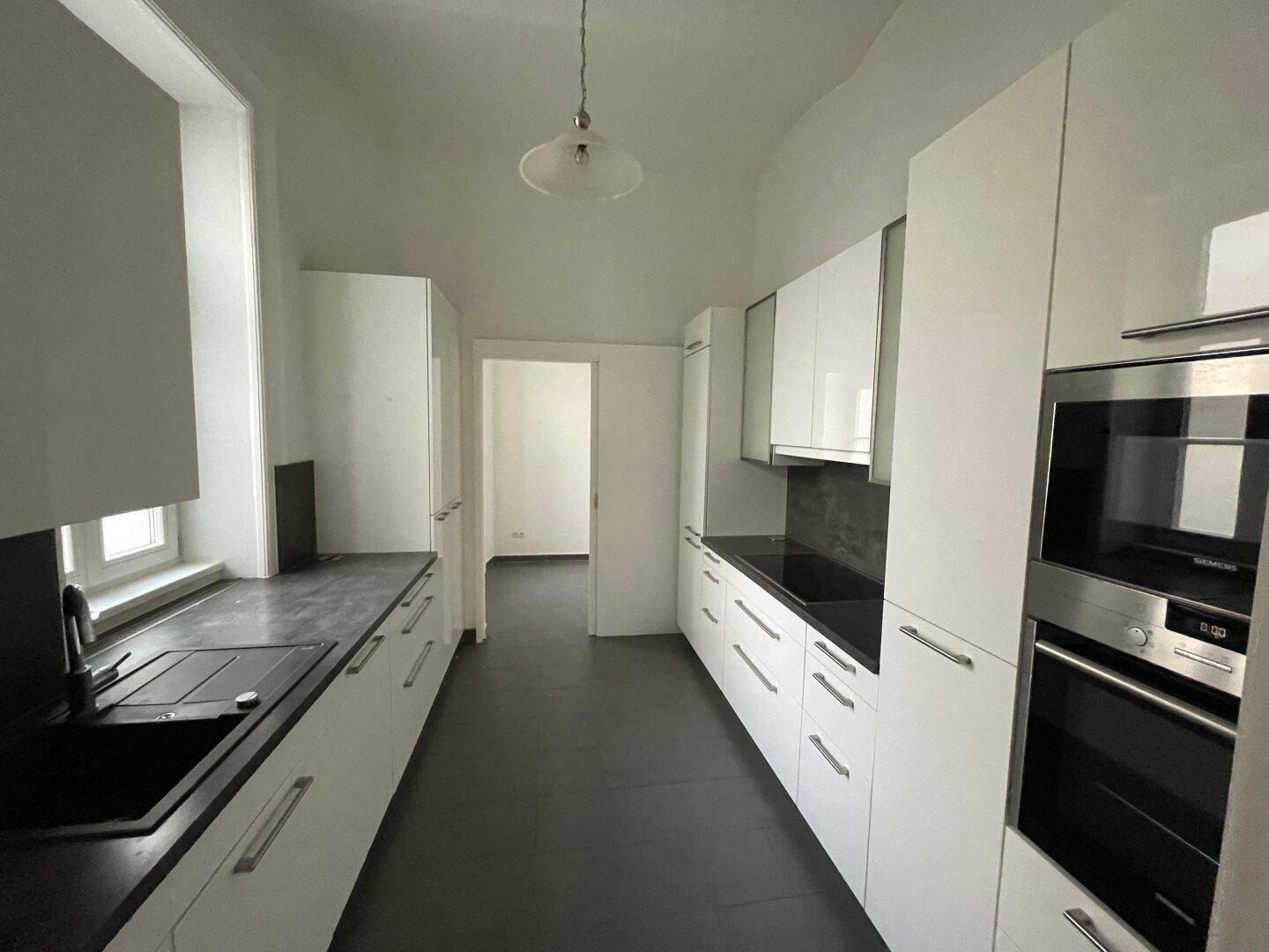 Moderne Küche mit weißen Hochglanzschränken, dunkler Arbeitsplatte und integrierten Geräten.