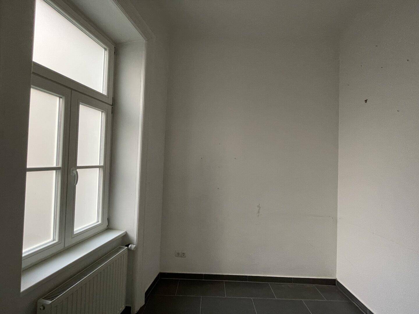 Kleiner, heller Raum mit Fenster und dunklem Fliesenboden, vielseitig nutzbar.