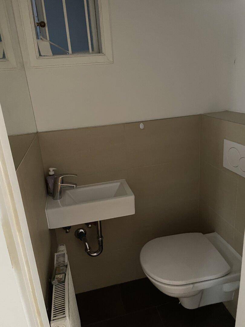 Kleines Gäste-WC mit Wand-WC, Waschbecken und Heizkörper.