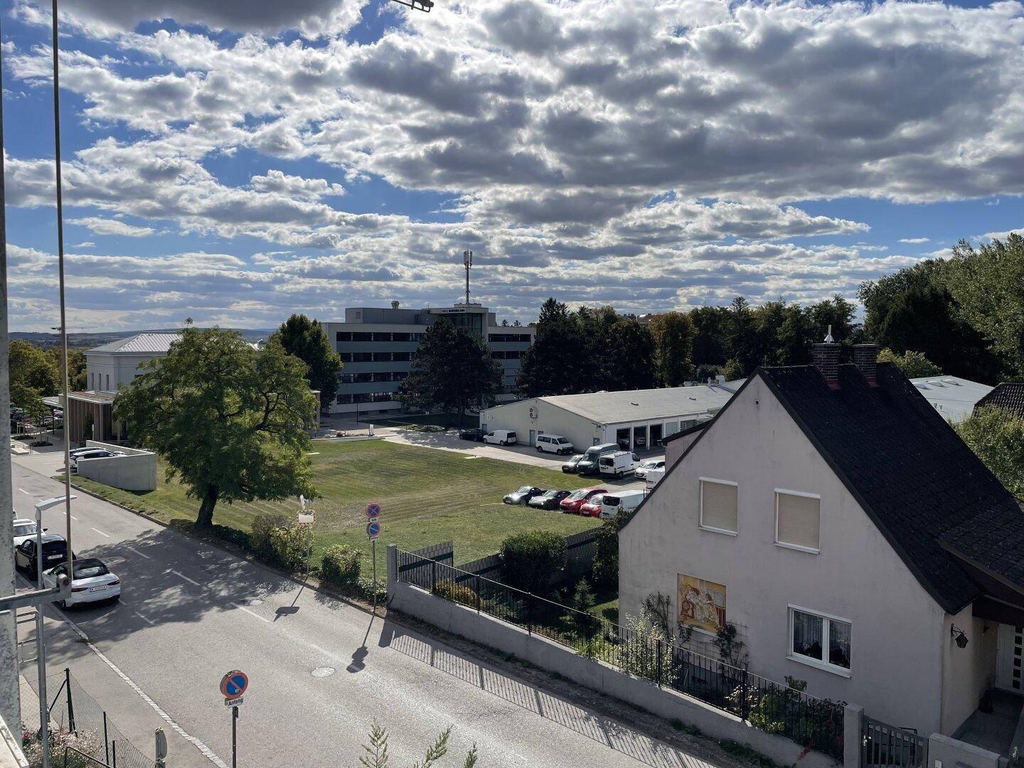 Weitläufiger Blick über eine Wohngegend mit Gebäuden, Bäumen und einem Parkplatz unter bewölktem Himmel.