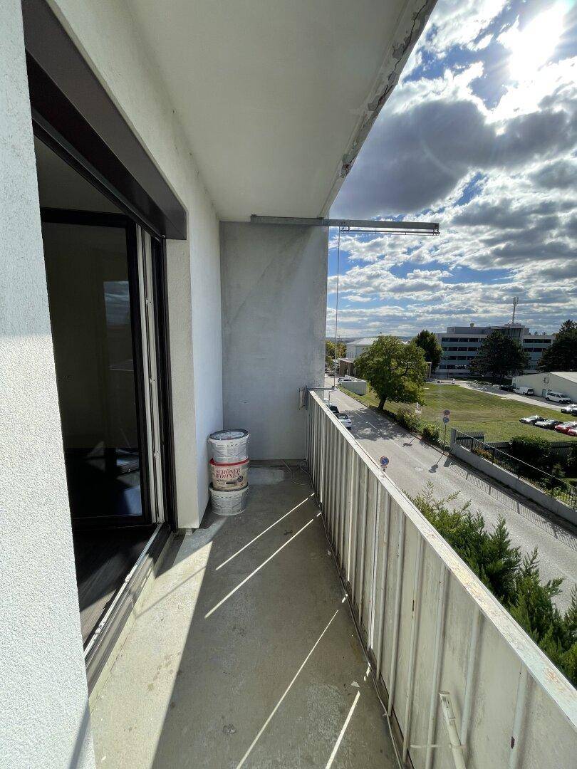 Schmaler Balkon mit Metallgeländer und Blick auf die Straße und umliegende Gebäude an einem sonnigen Tag.