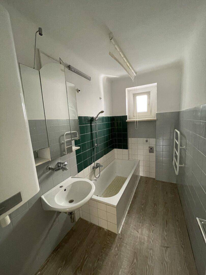 Badezimmer mit Badewanne, Waschbecken und Fliesen in Grün- und Grautönen, inklusive Fenster.