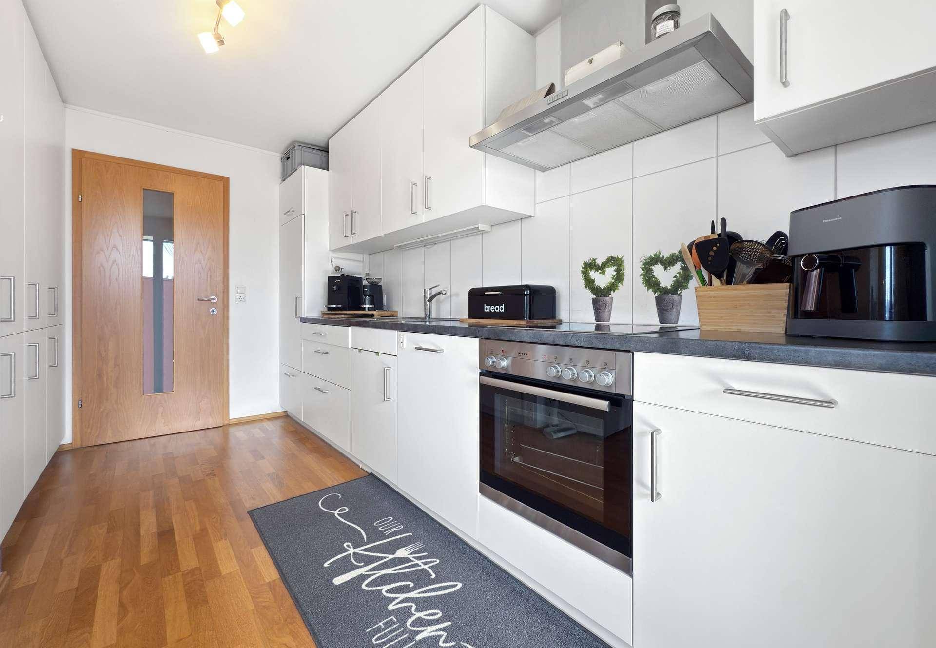 Moderne weiße Küche mit Holzboden, integriertem Backofen und viel Stauraum.
