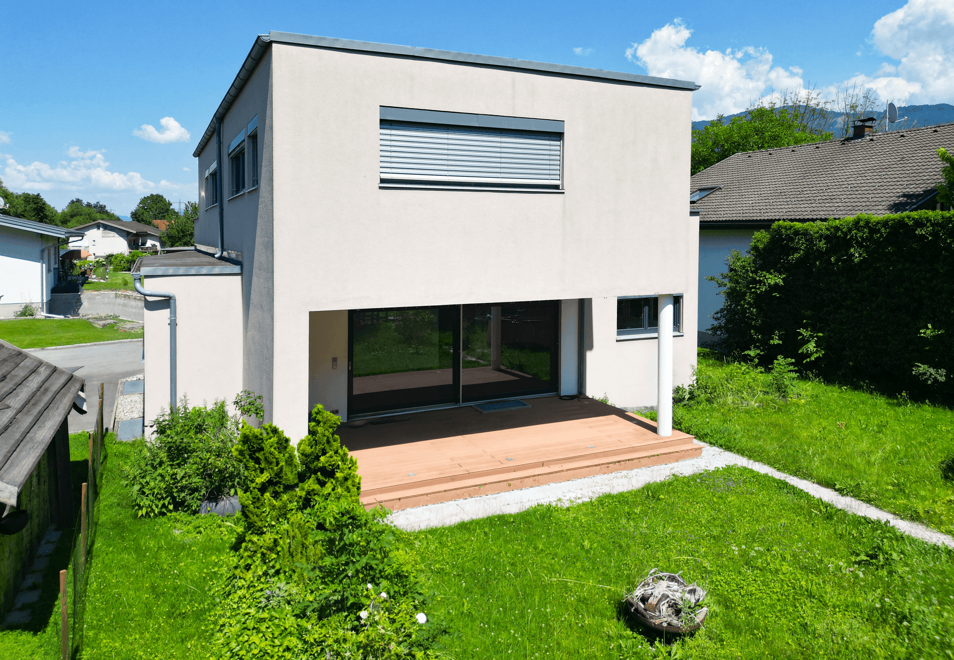 Moderne Hausfassade mit großer Holzterrasse und direktem Zugang zum Garten.