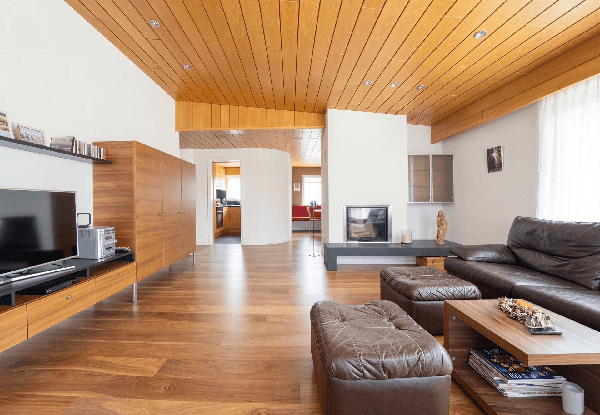 Helles Wohnzimmer mit Holzboden, Kamin und Zugang zu weiteren Räumen.