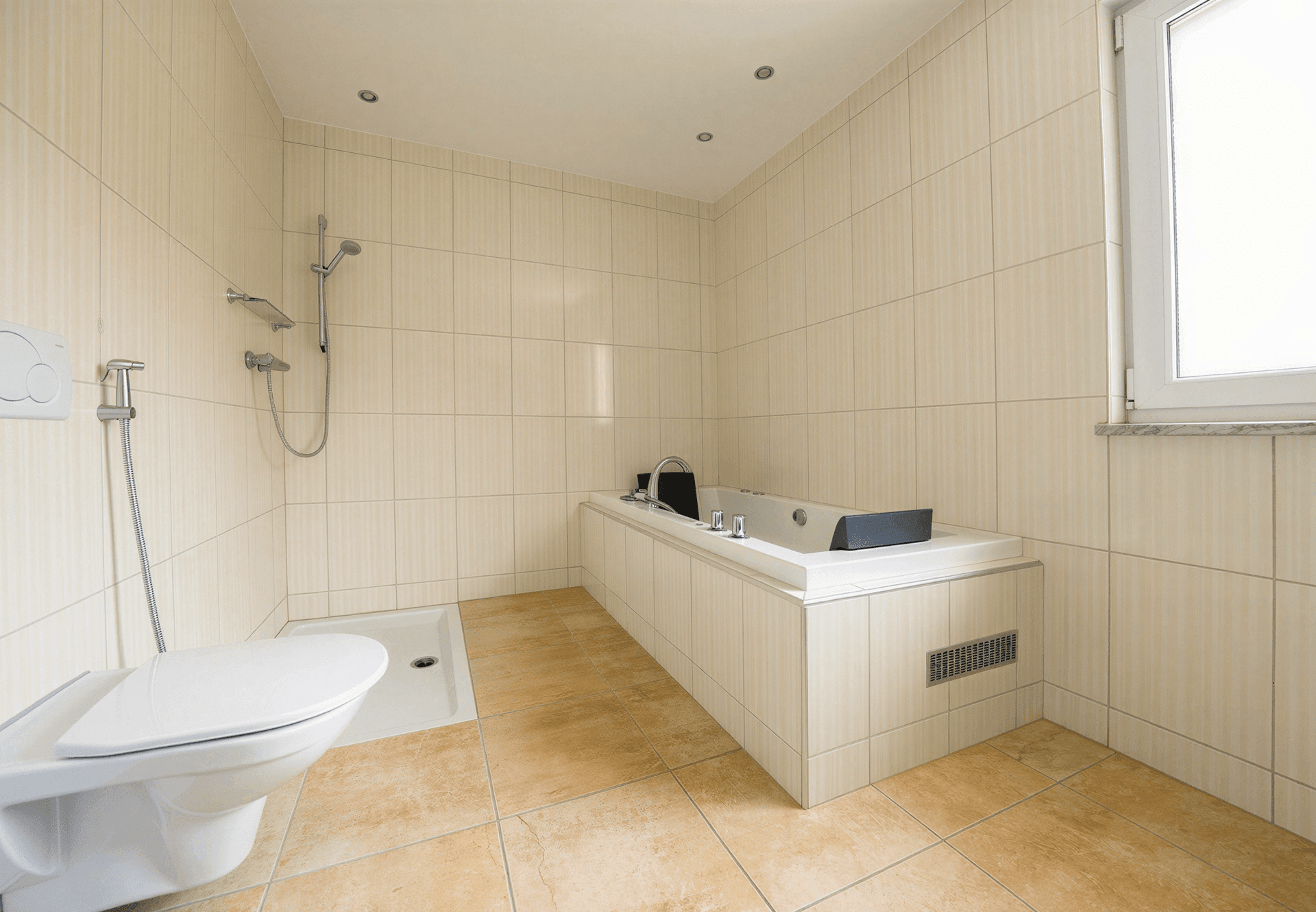 Geräumiges Badezimmer mit beigen Fliesen, Badewanne, Dusche und WC, mit Fenster für Tageslicht.