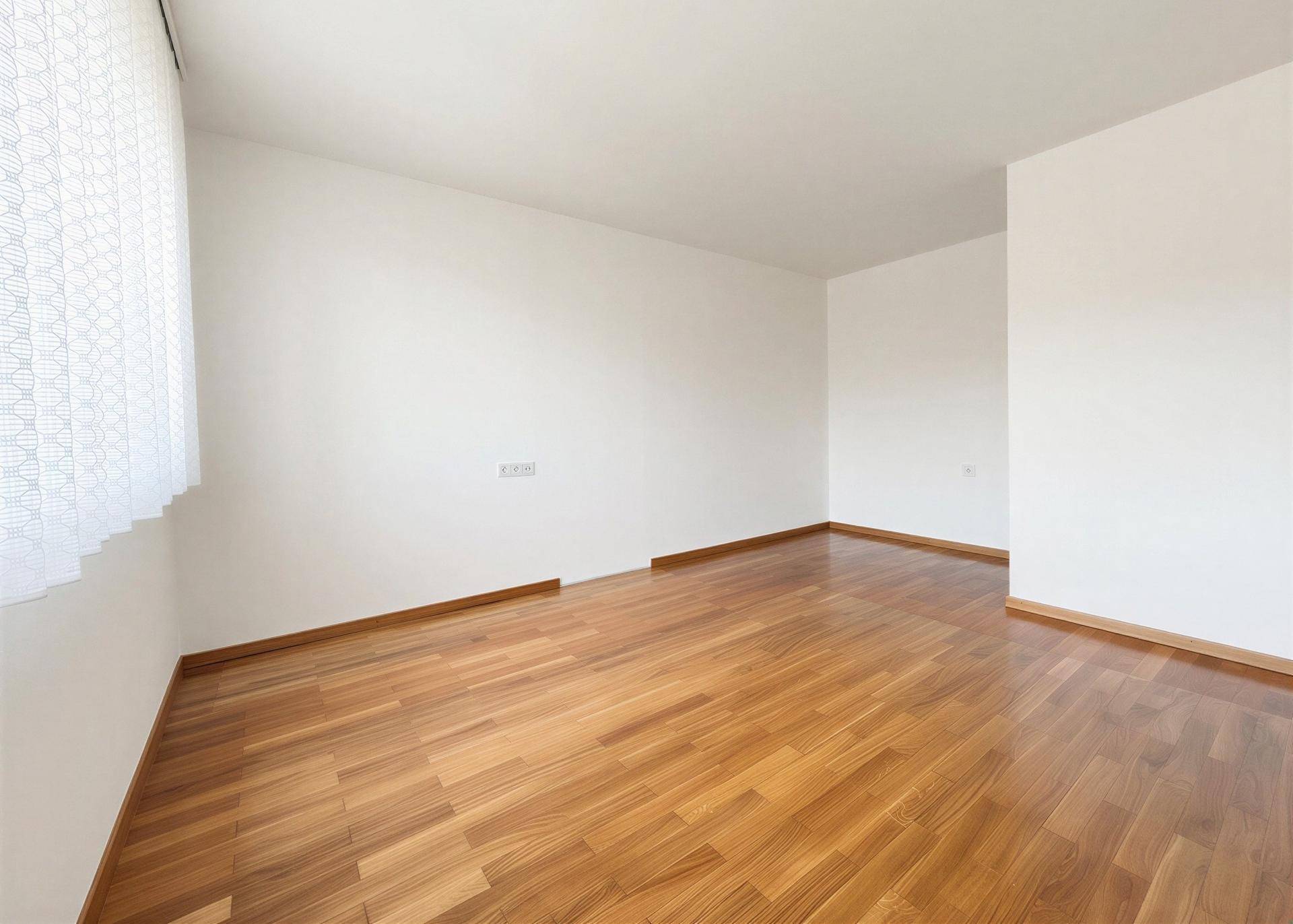 Helles, leeres Zimmer mit Holzboden und weiß gestrichenen Wänden.