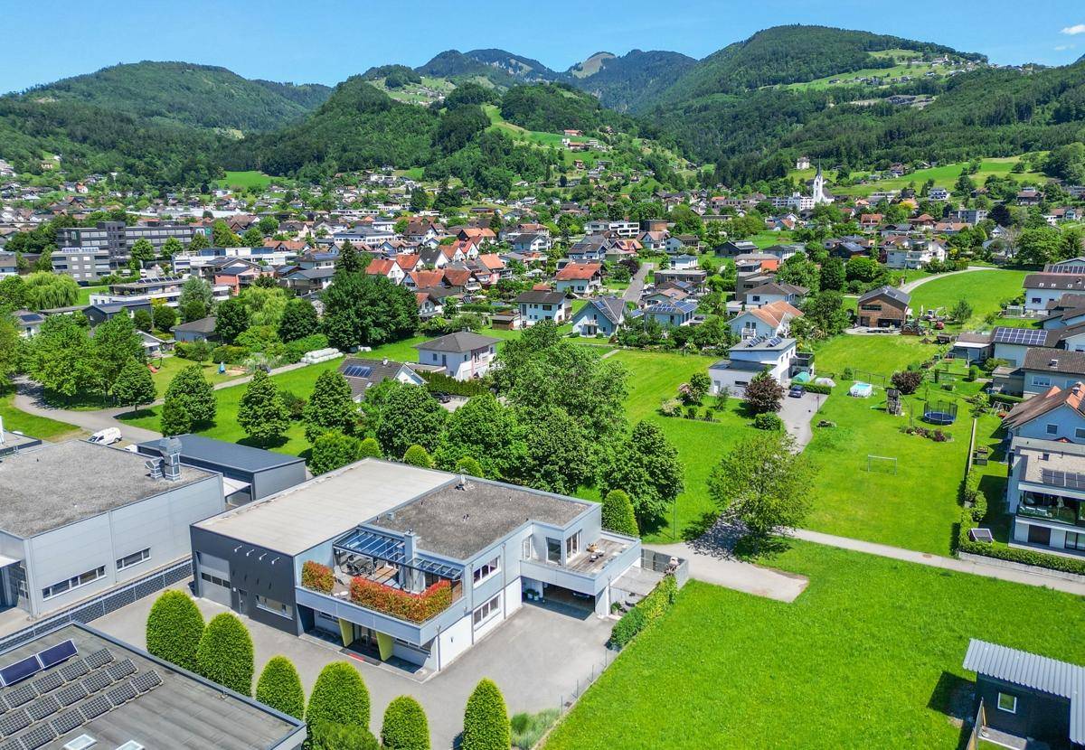 Weitläufige Luftaufnahme eines Gewerbegebiets mit angrenzenden Wohngebieten und Bergen im Hintergrund.