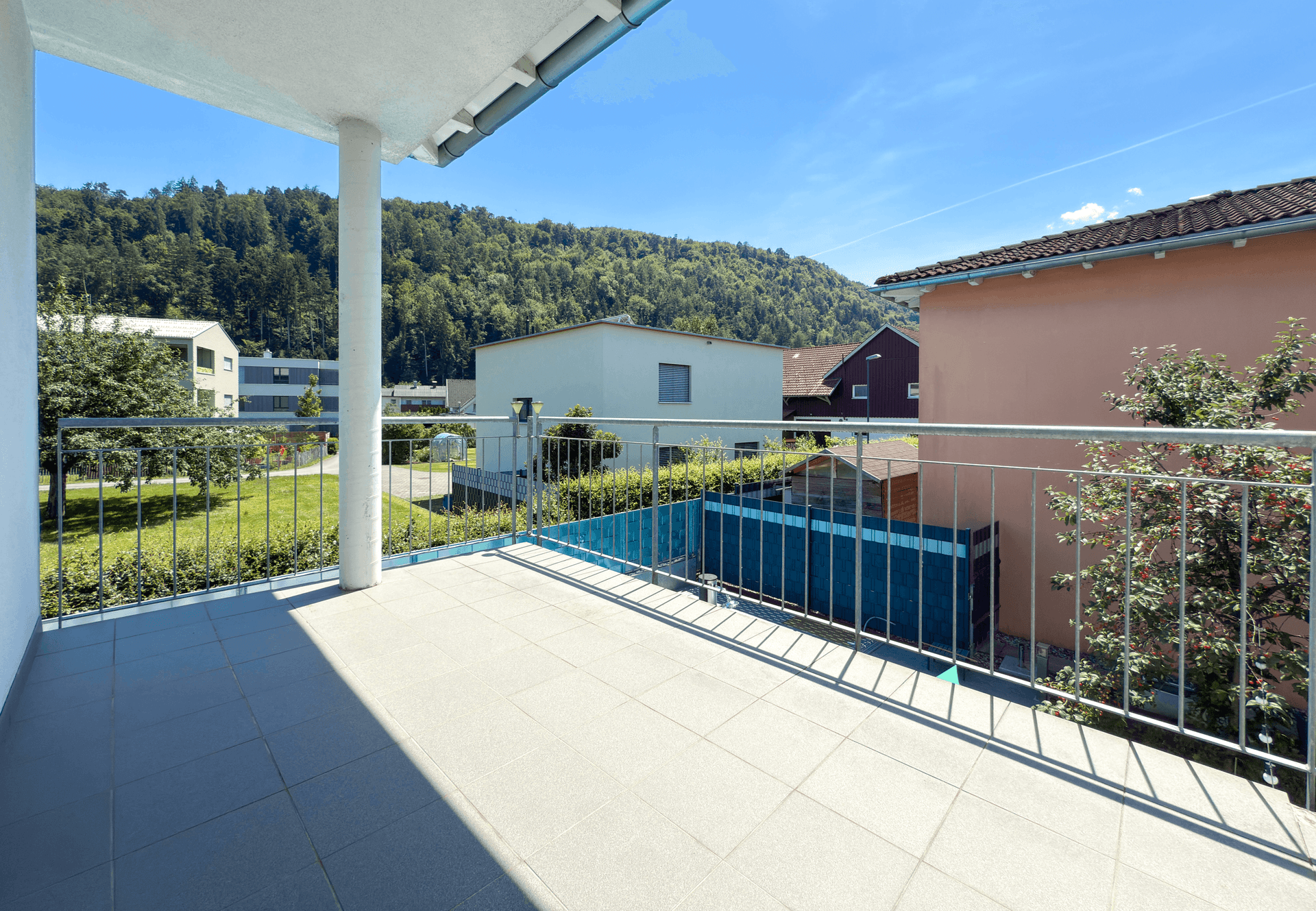 Geräumiger Balkon mit Fliesenboden und weitem Blick auf die grüne Umgebung und Berge.