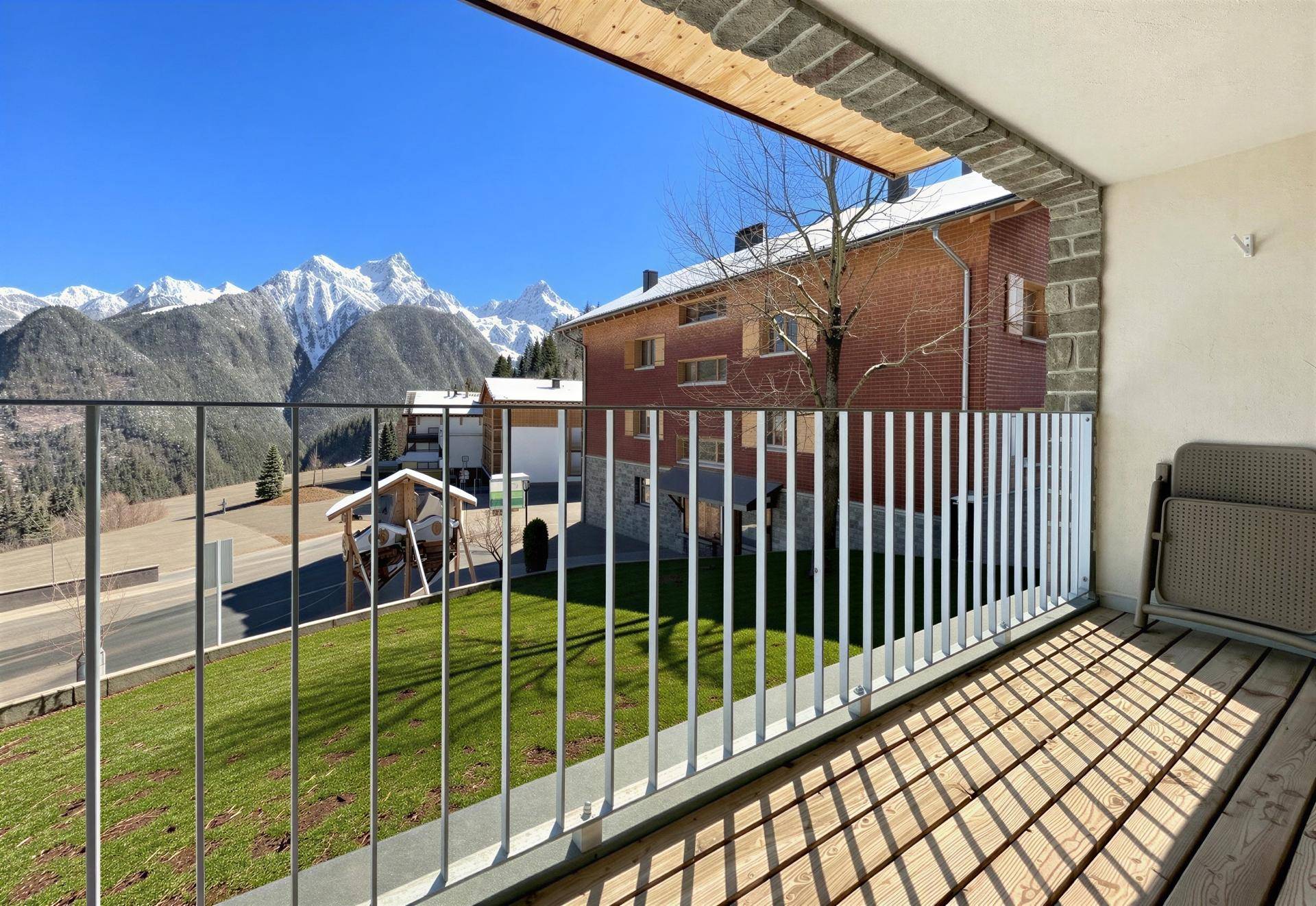 Sonniger Balkon mit Holzboden und weitem Blick auf die Berge und die umliegende Landschaft.