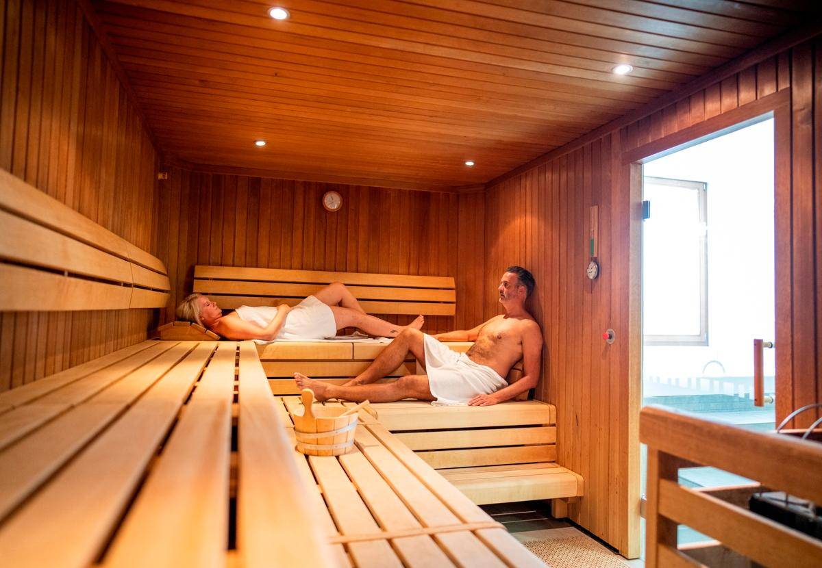 Geräumige Holzsauna mit Bänken und entspannenden Personen, Teil des Wellnessbereichs.
