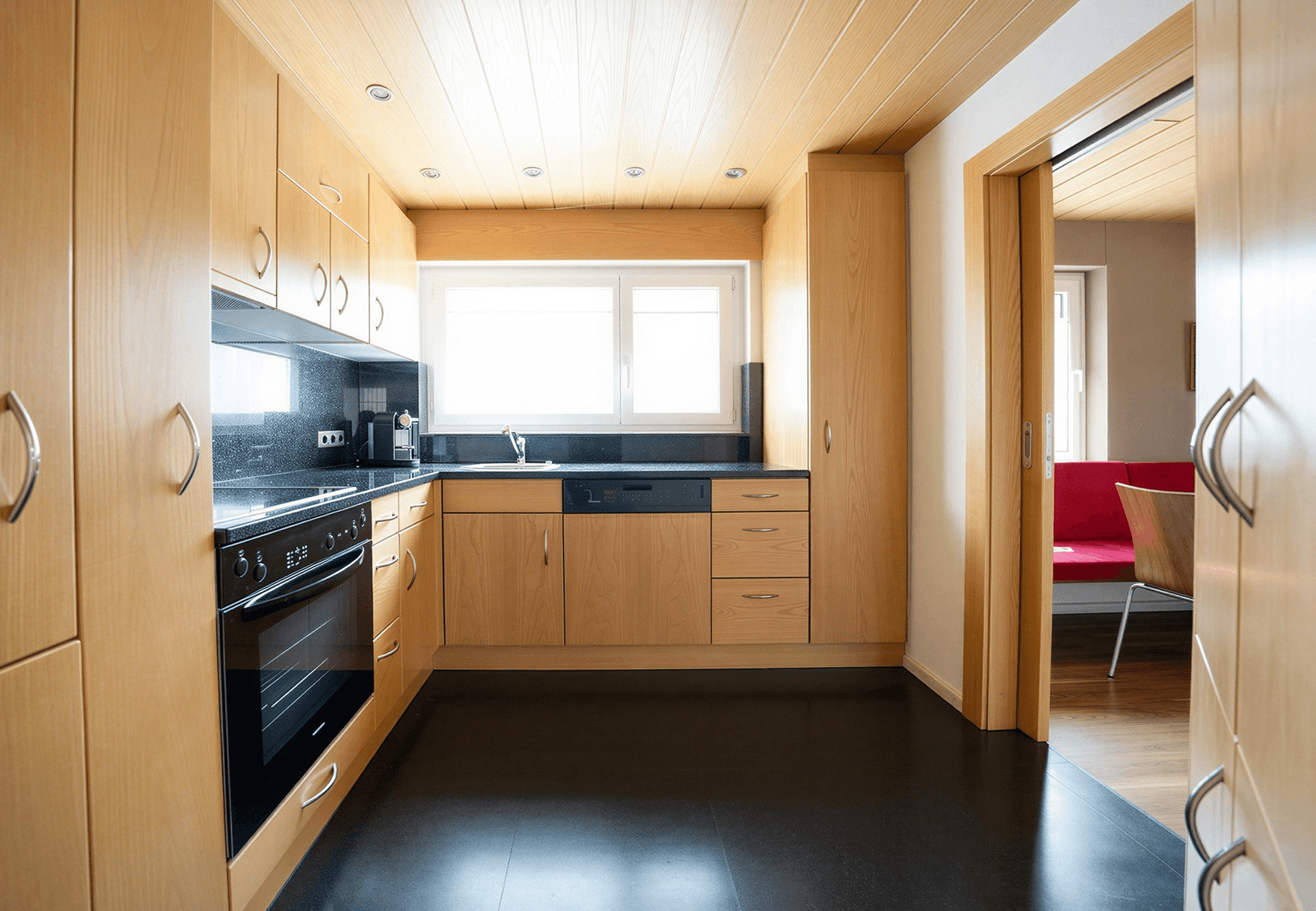 Funktionale Küche mit hellen Holzschränken, dunkler Arbeitsplatte und Fenster.