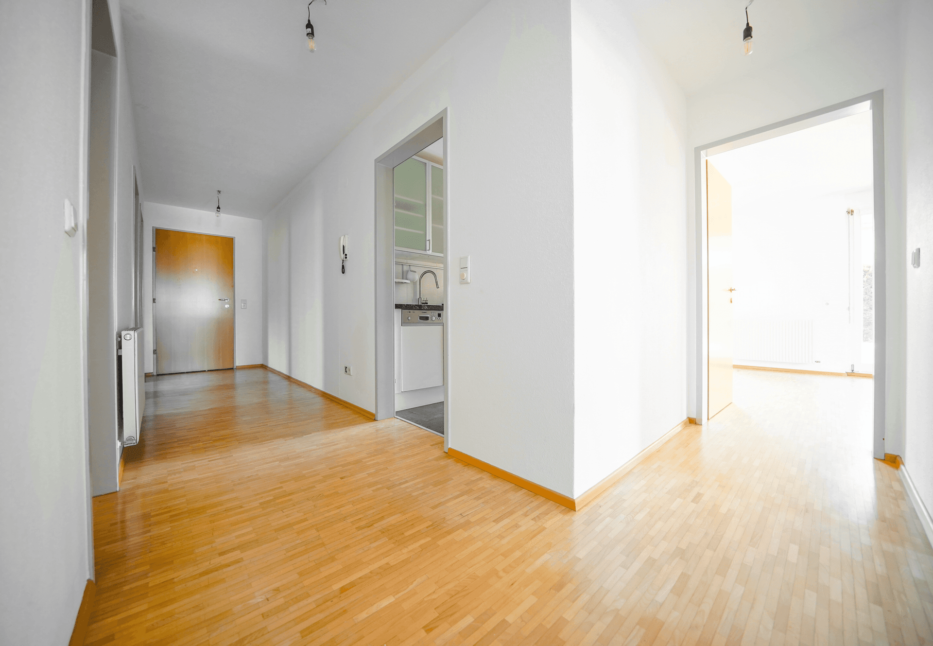 Heller Flur mit Holzboden und Zugang zu verschiedenen Räumen, inklusive kleiner Kochnische.