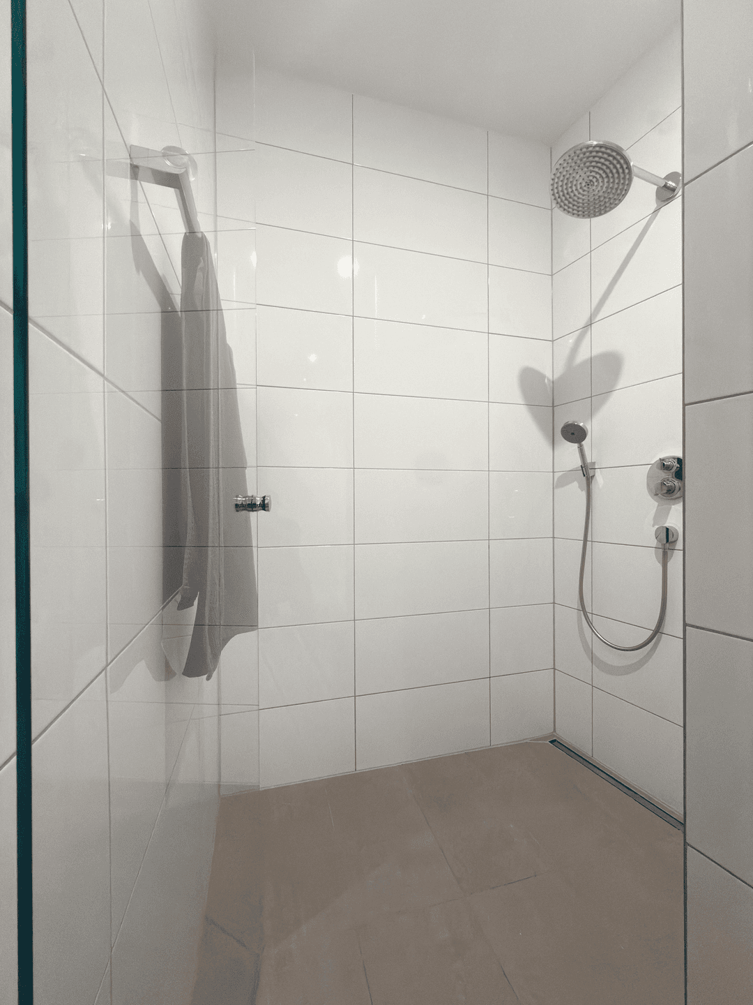Geräumige, ebenerdige Dusche mit modernen weißen Fliesen und Regenduschkopf.