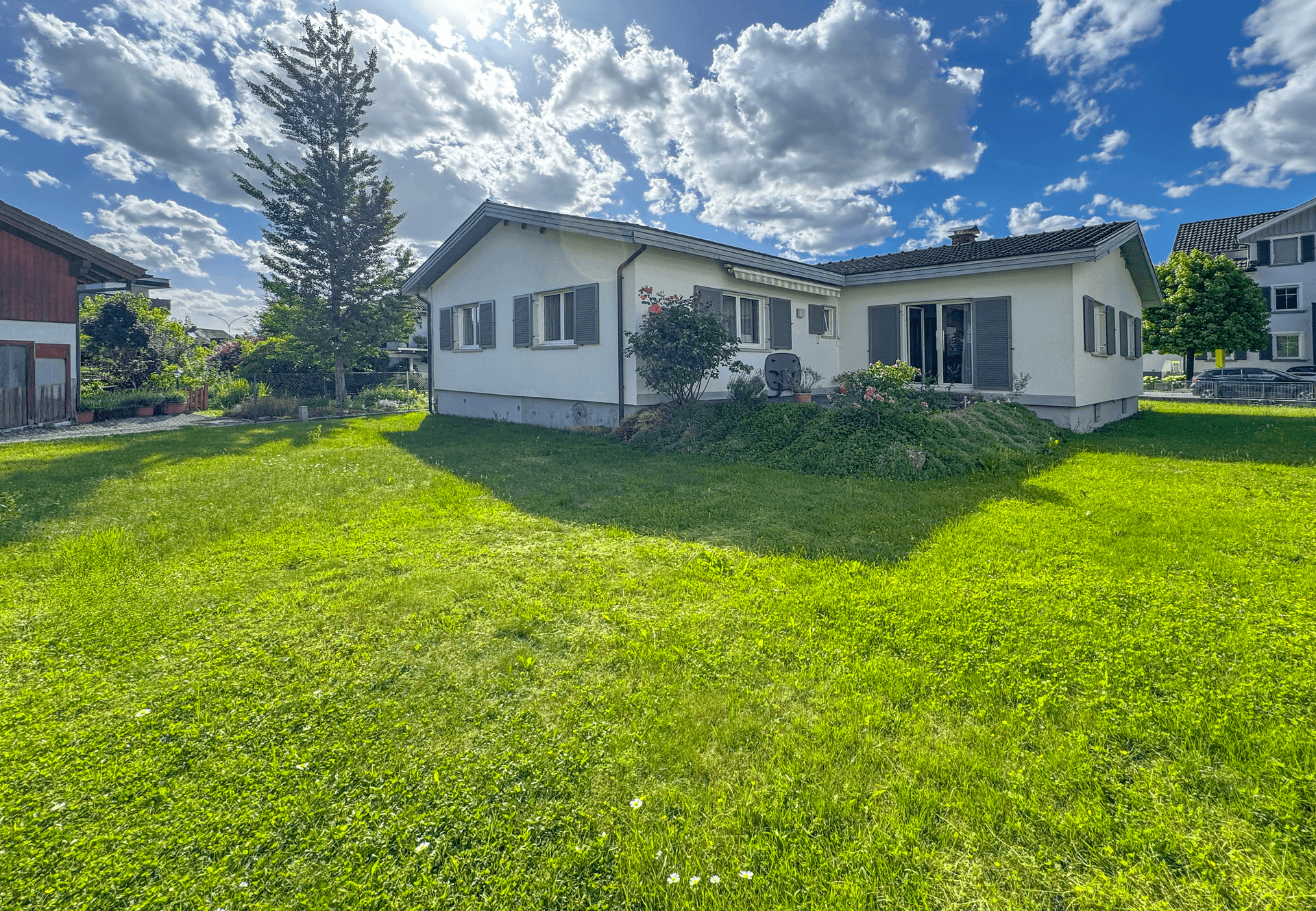 Rückansicht des Hauses vom weitläufigen Garten aus, umgeben von viel Grün und Sonnenschein.