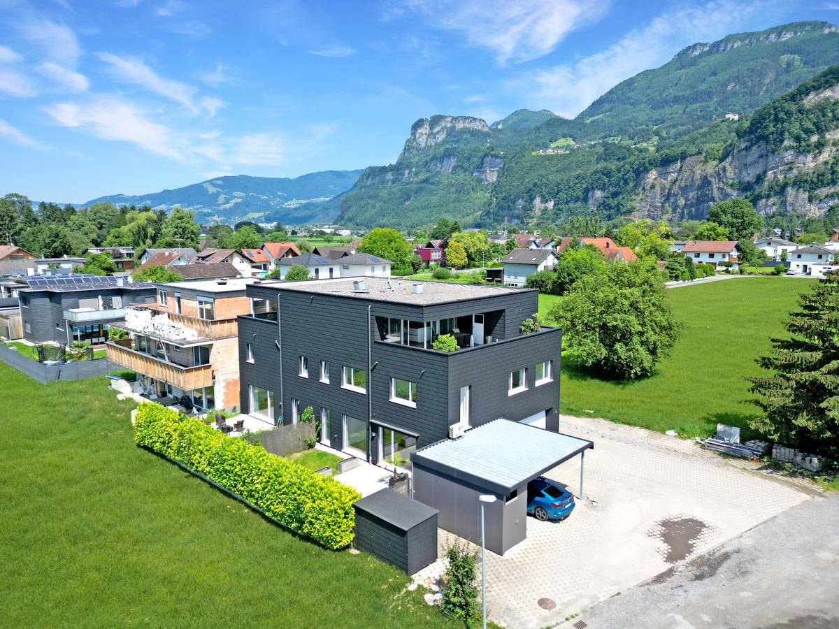 Luftaufnahme eines modernen Gebäudes mit Carport, umgeben von Natur und Bergen.