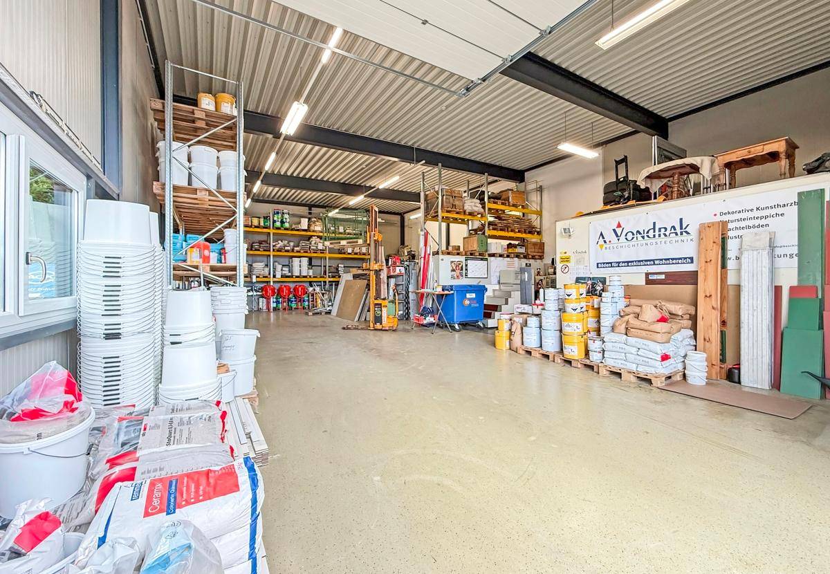Geräumiges Lager mit hohen Regalen, verschiedenen Materialien und Produkten sowie einem großen Rolltor.