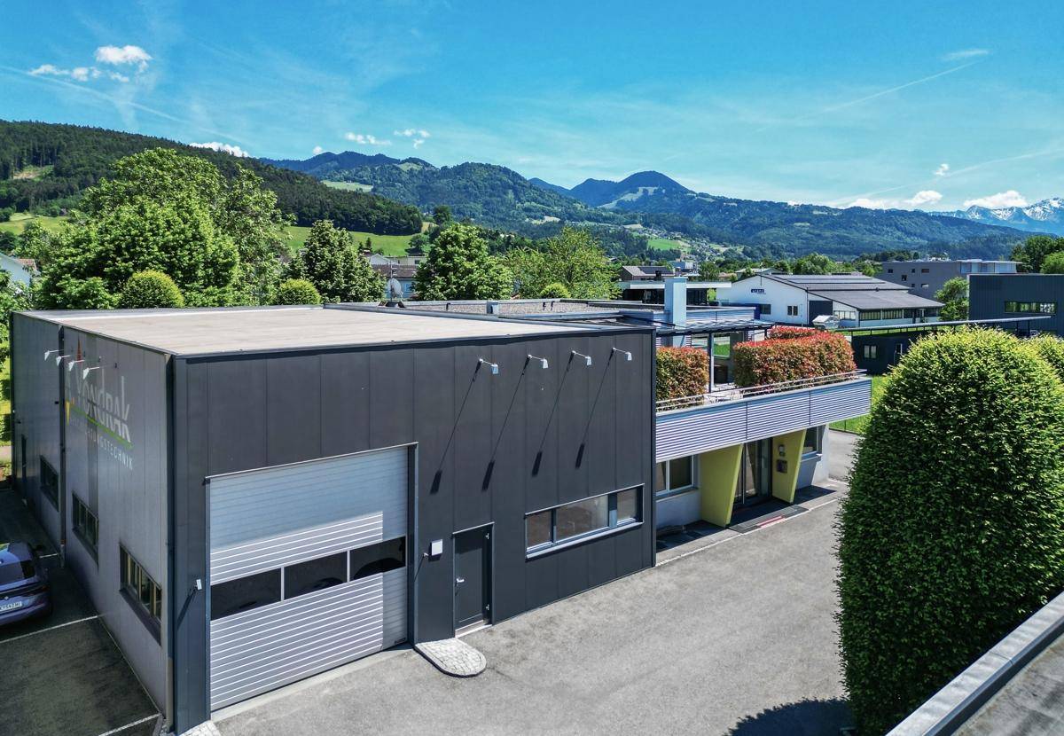 Moderne Gewerbeimmobilie mit Flachdach, großen Fenstern und einer begrünten Terrasse.