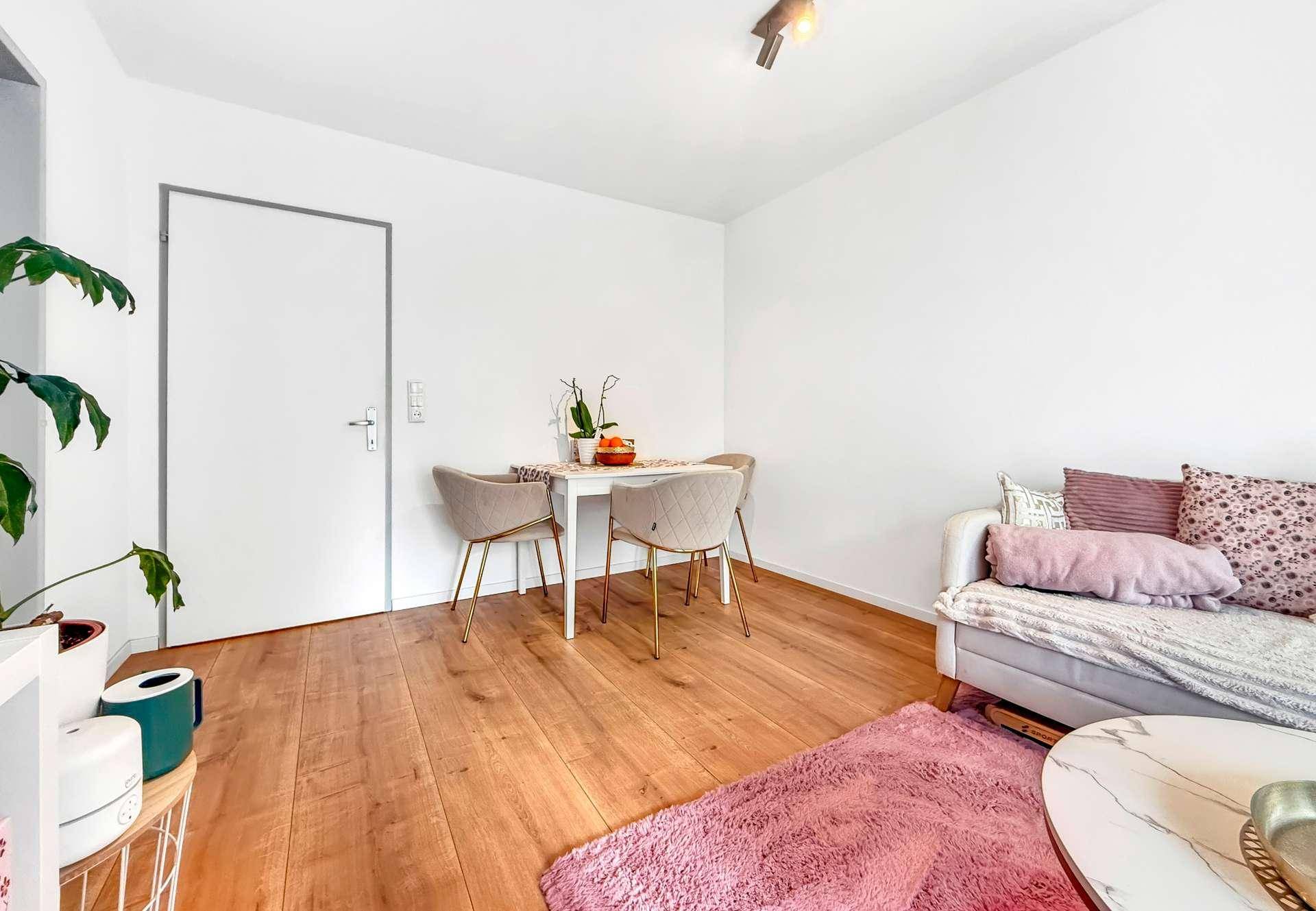 Essbereich mit kleinem Tisch und Stühlen, angrenzend an den Wohnbereich mit Holzboden.