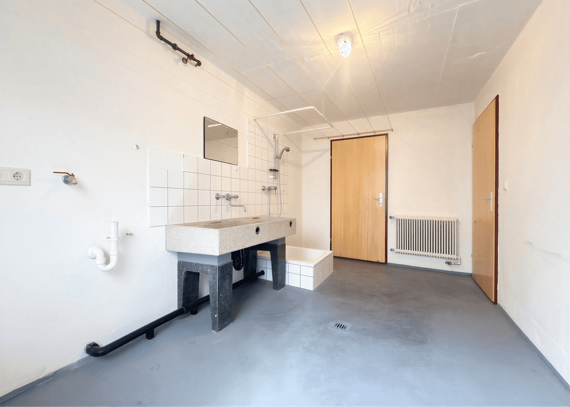Waschküche im Keller mit Waschbecken, Dusche und Betonboden.