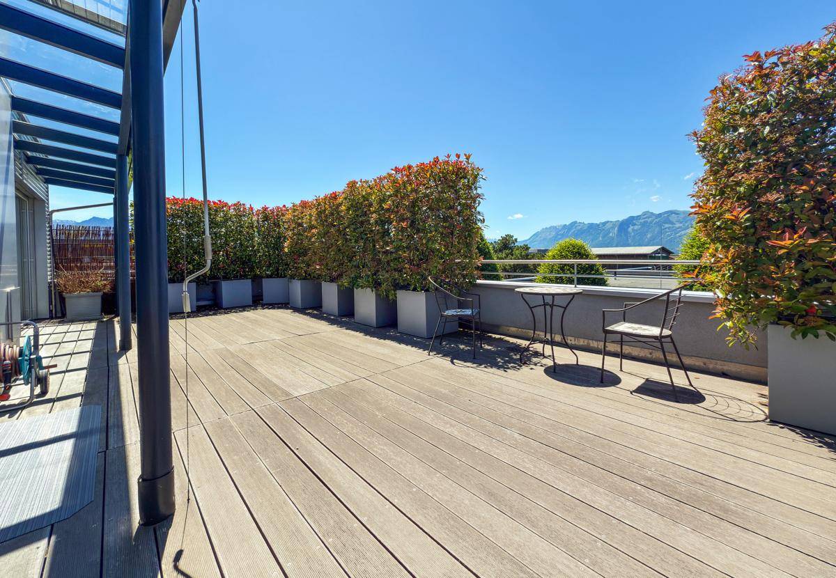 Weitläufige Dachterrasse mit Holzplanken, hohen Pflanzenkübeln und einem weiten Blick auf die Berge.